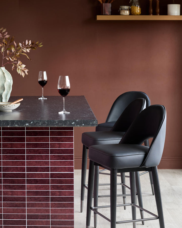 A stylish bar area with two black bar stools, a black countertop, and a decorative tiled panel.