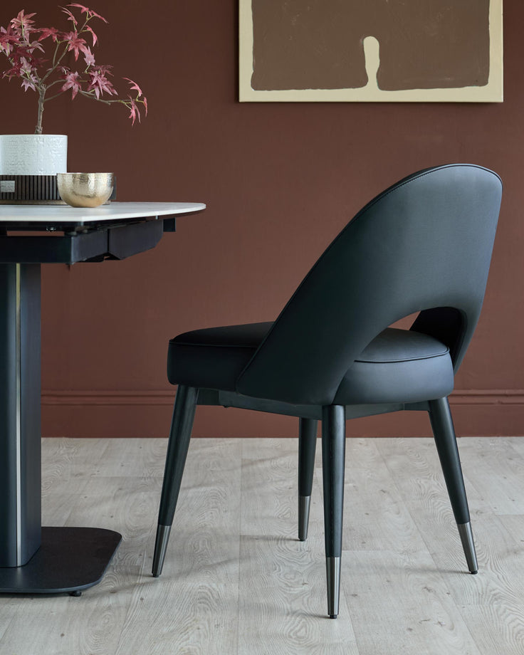 A black dining chair is positioned beside a modern dining table against a brown wall, creating a stylish and inviting setting.