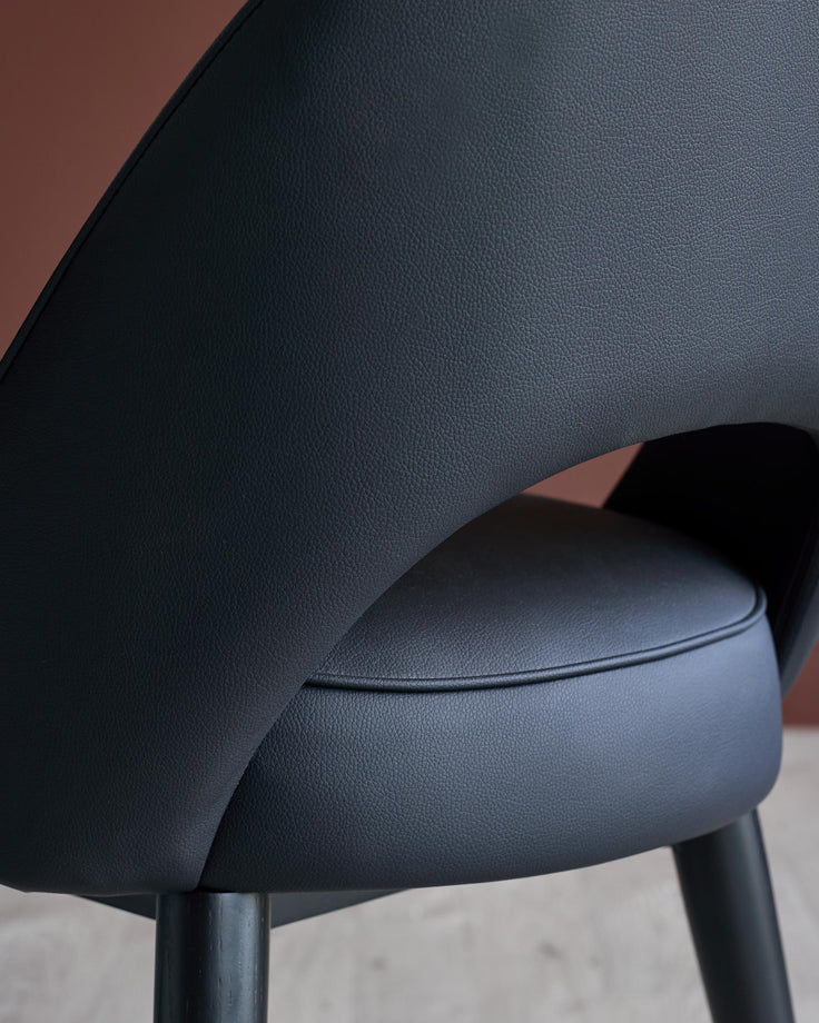 Close-up of a modern black leather chair with a curved back and round seat. The chair legs are also black.
