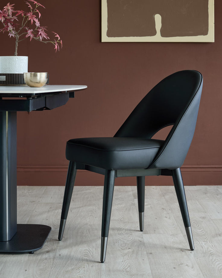 A stylish black dining chair sits next to a modern table, showcasing contemporary furniture design.