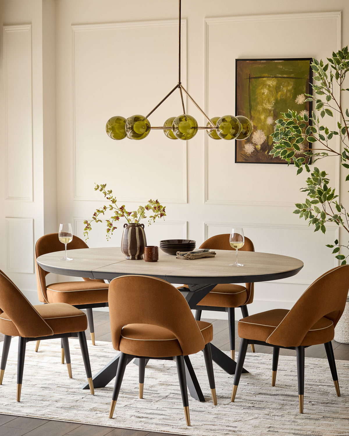 Hayden round extending dining table in natural travertine with black metal base, styled in dining room setting with caramel velvet chairs.