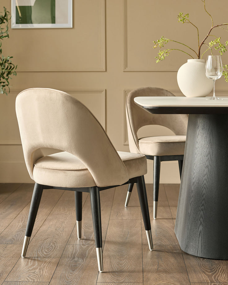 Clover velvet dining chair in champagne with black legs and stainless steel caps, shown at a round table.