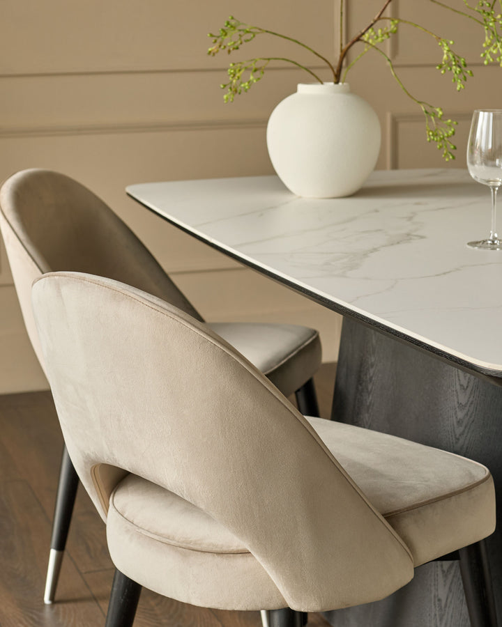 Champagne velvet dining chair with curved back and black legs, shown at marble table setting.