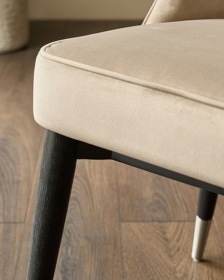 Clover dining chair detail showing cream velvet upholstery, dark wood legs, and stainless steel cap feet.