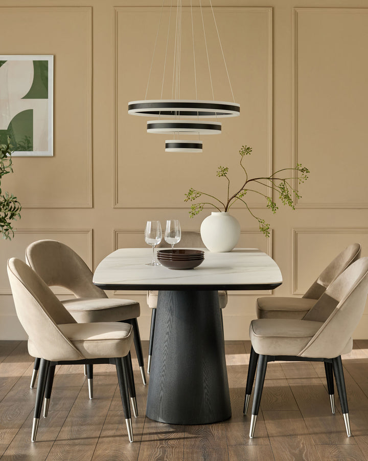 Champagne velvet dining chair with curved back, black legs, and stainless steel foot caps, shown in dining room setting.