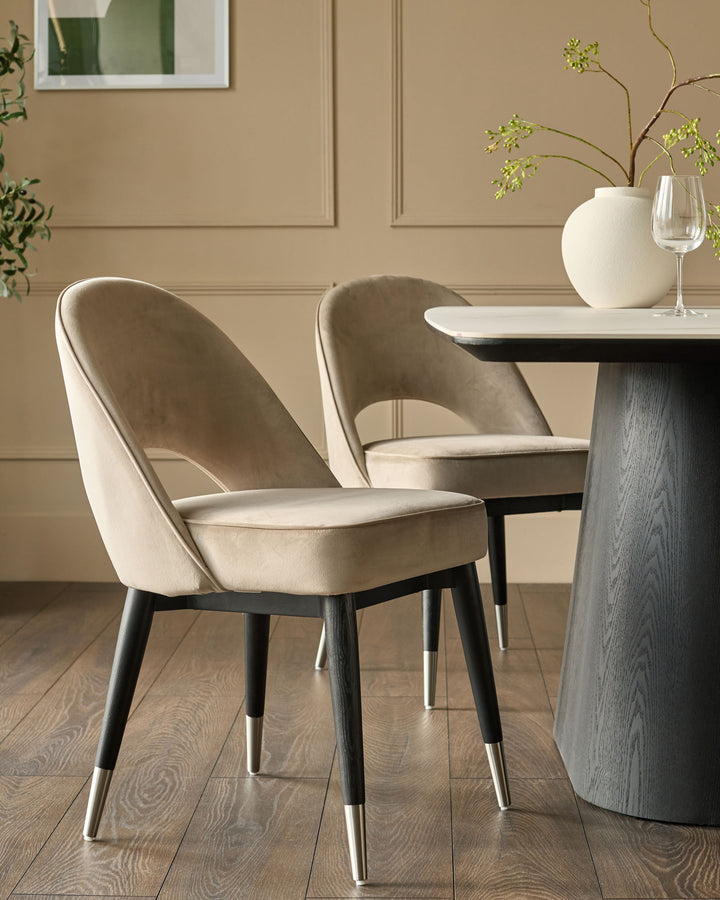 Champagne velvet dining chair with curved back, black wooden legs, and stainless steel caps, shown at table setting.