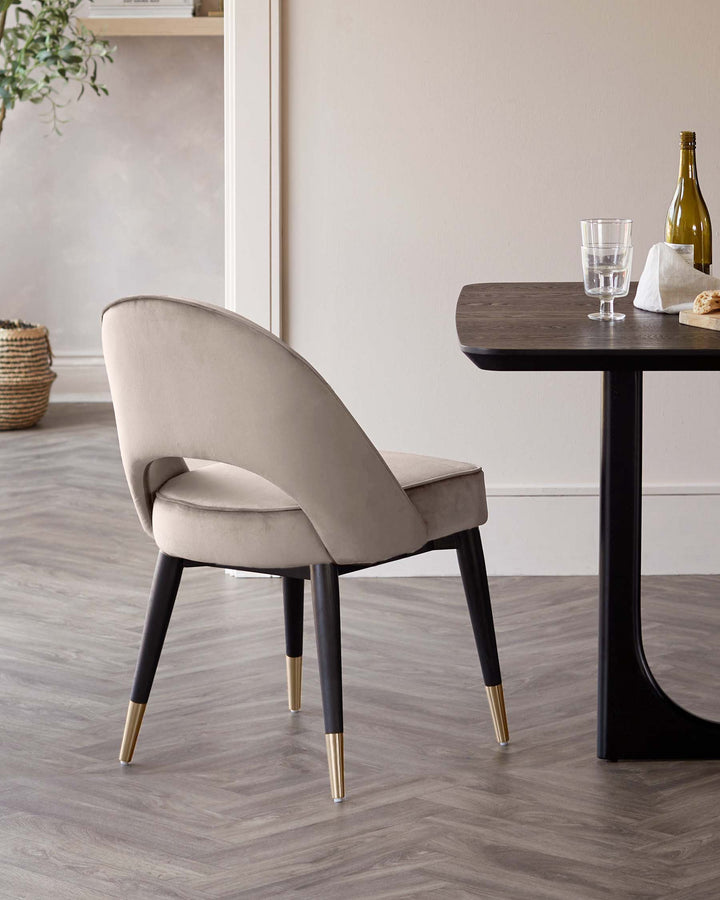 Upholstered chair with black legs and gold accents next to a dark wood table, creating a contemporary dining area.