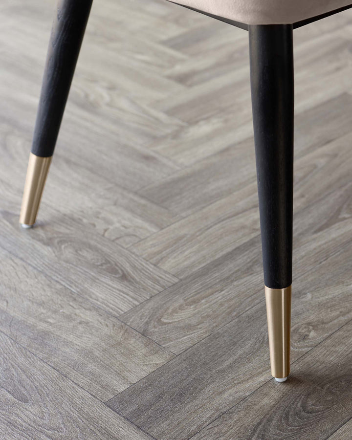Close-up of furniture legs with gold-tone accents against a herringbone-patterned floor, exuding modern elegance.