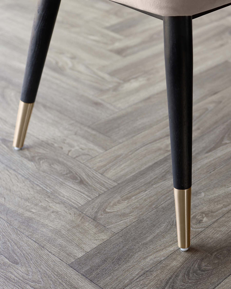 Close-up of furniture legs with gold-tone accents against a herringbone-patterned floor, exuding modern elegance.