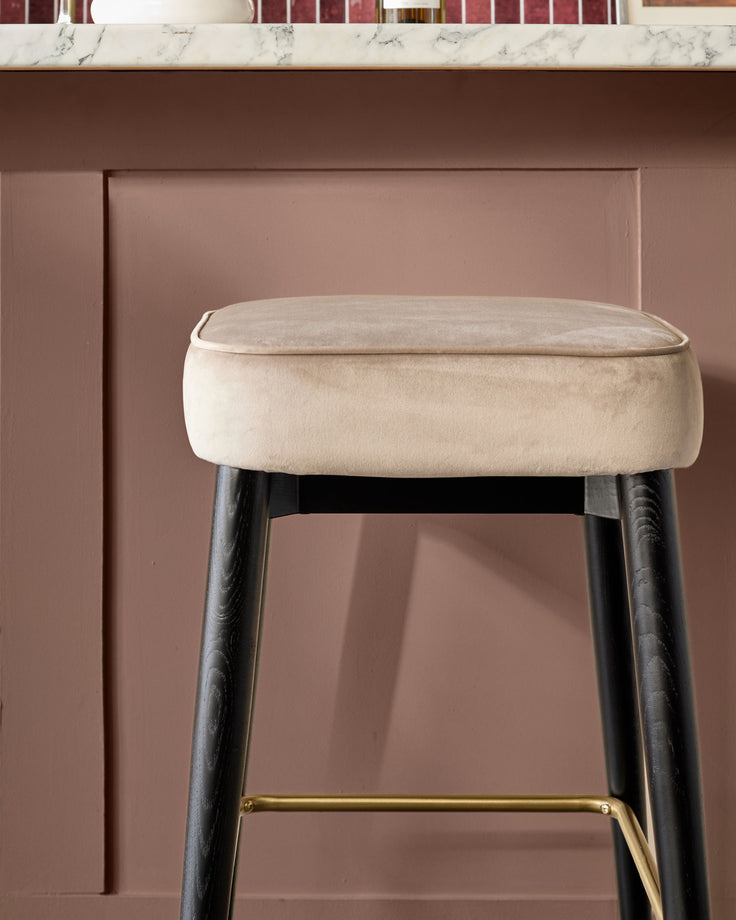 Clover velvet backless bar stool in champagne with black wooden legs and brass footrest.