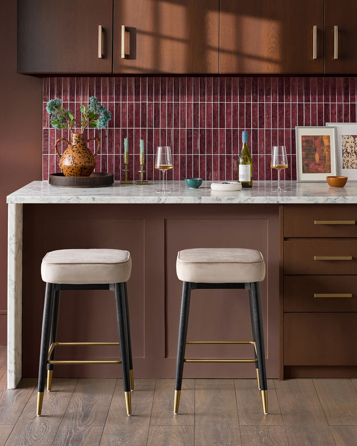 Champagne velvet backless bar stools with black legs and brass footrests, shown as a pair at a marble kitchen island.