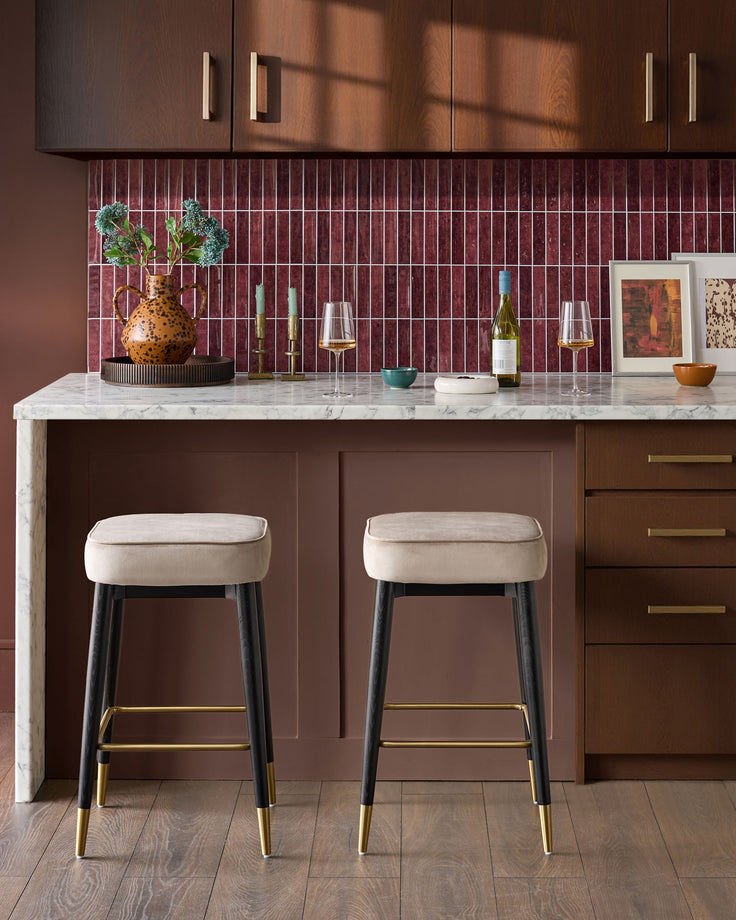 Champagne velvet backless bar stools with black legs and brass footrests, shown as a pair at a marble kitchen island.