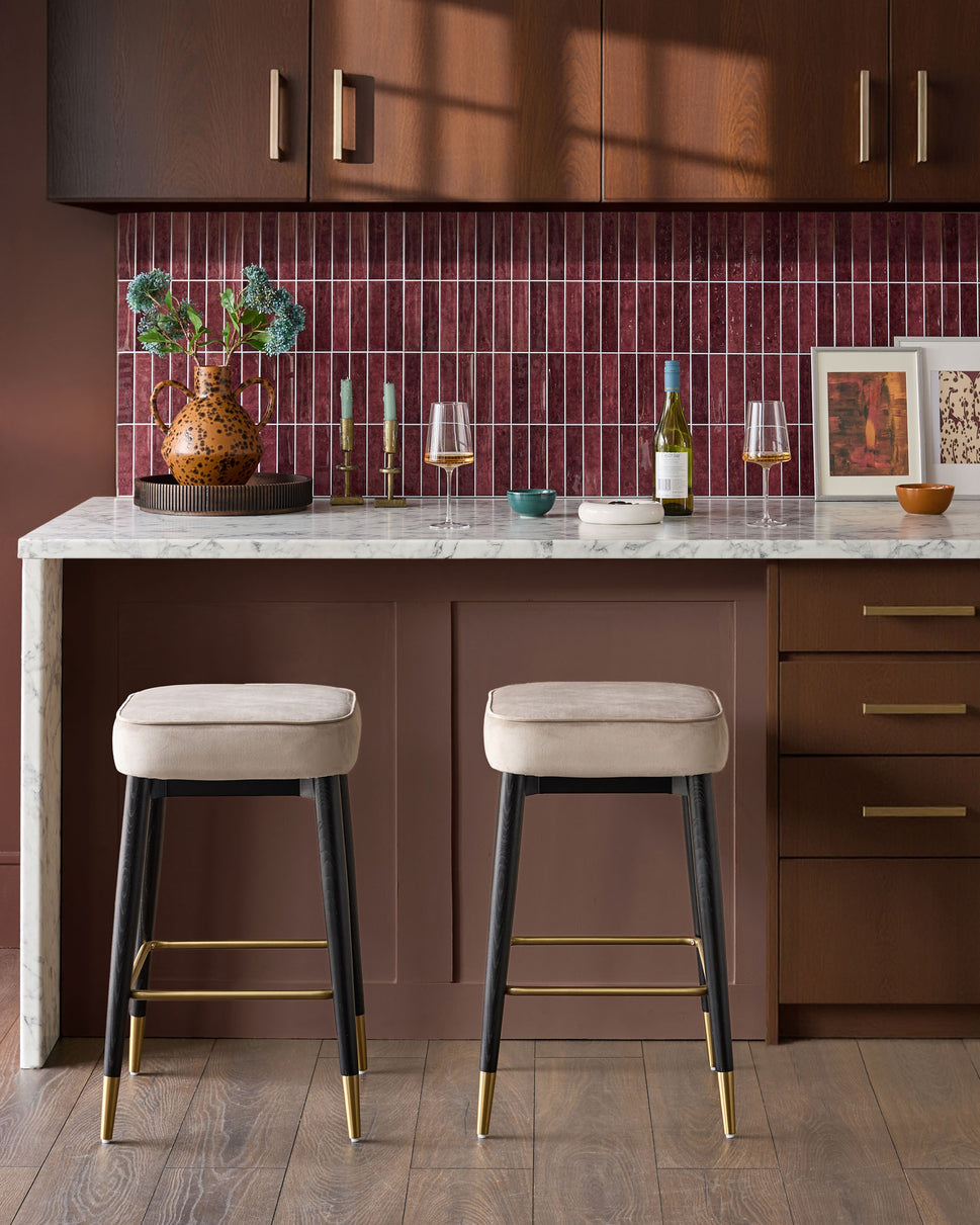 Champagne velvet backless bar stools with black legs and brass footrests, shown as a pair at a marble kitchen island.