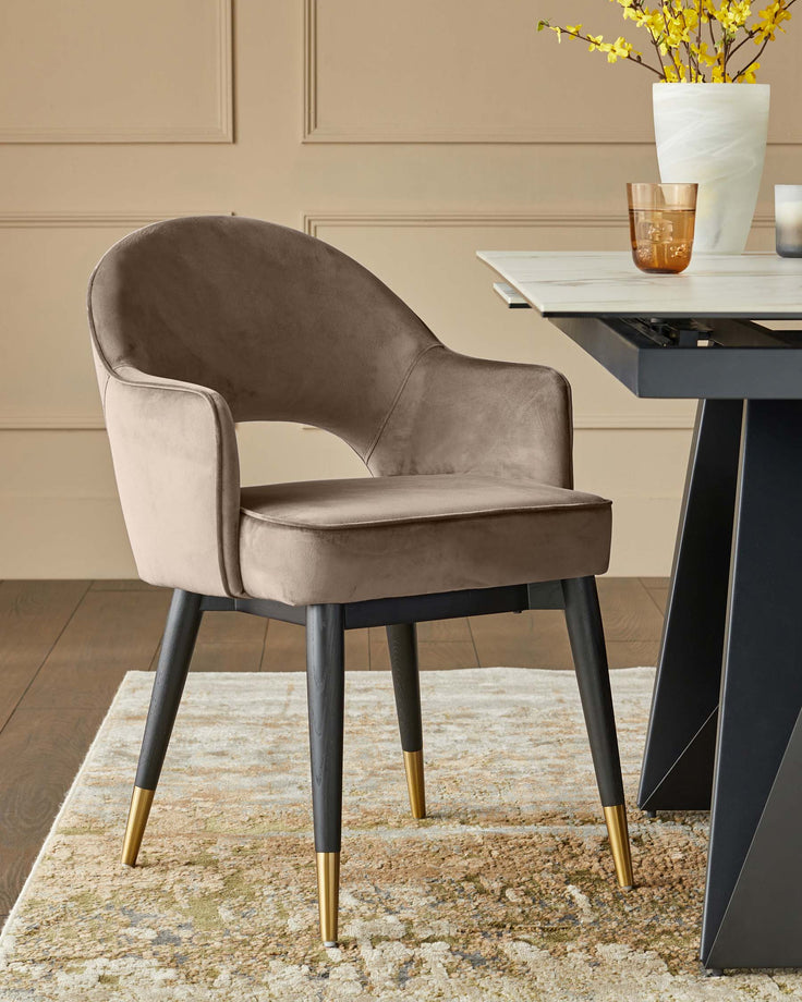 A plush brown chair with gold capped legs sits on a patterned rug next to a table with flowers.