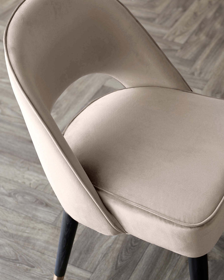 Close-up of an upholstered dining chair in a neutral colour with dark wooden legs and a gold accent.