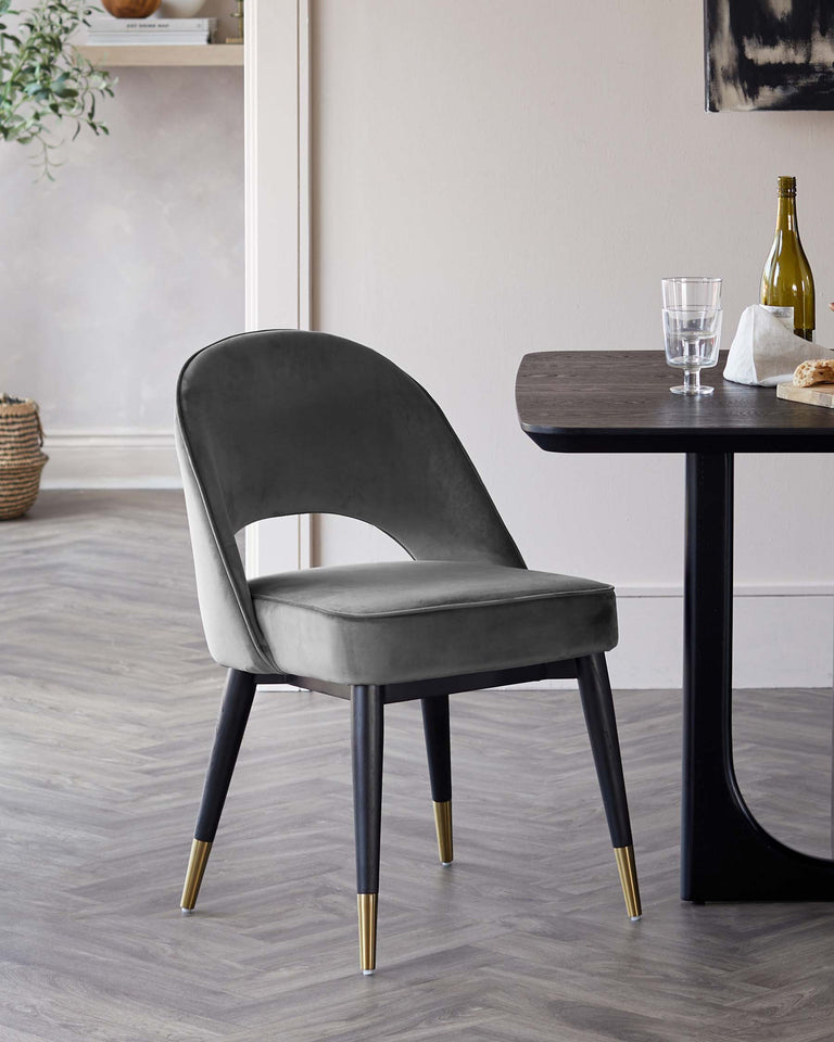 Elegant modern dining chair with plush grey velvet upholstery and black wooden legs tipped with gold accents, paired with a sleek black wooden dining table.