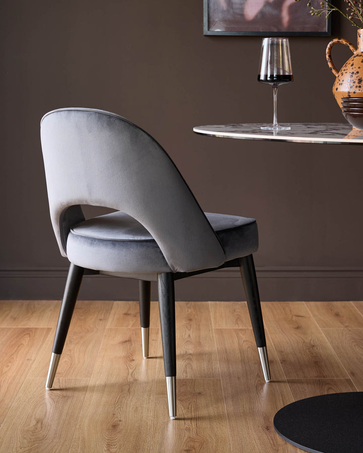 Dark grey velvet dining chair with curved backrest and stainless steel leg caps, shown from rear angle.