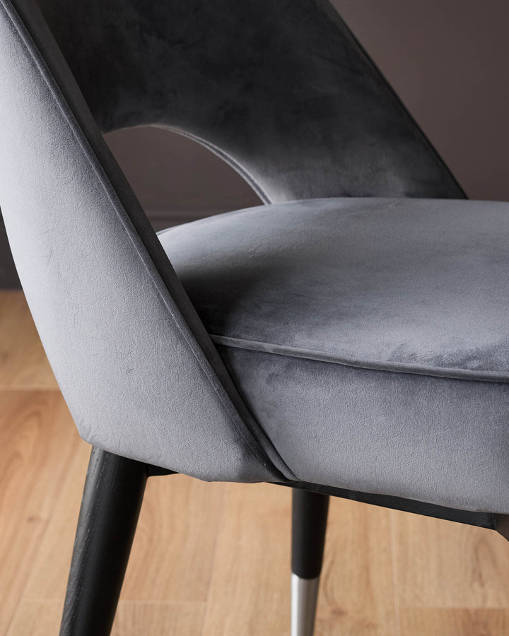 Clover velvet dining chair in dark grey with black legs and stainless steel caps, side angle view on wooden floor.