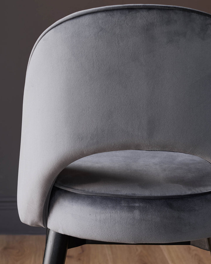 Dark grey velvet dining chair with curved backrest and black legs, side angle view.
