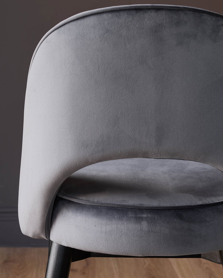 Dark grey velvet dining chair with curved backrest and black legs, side angle view.