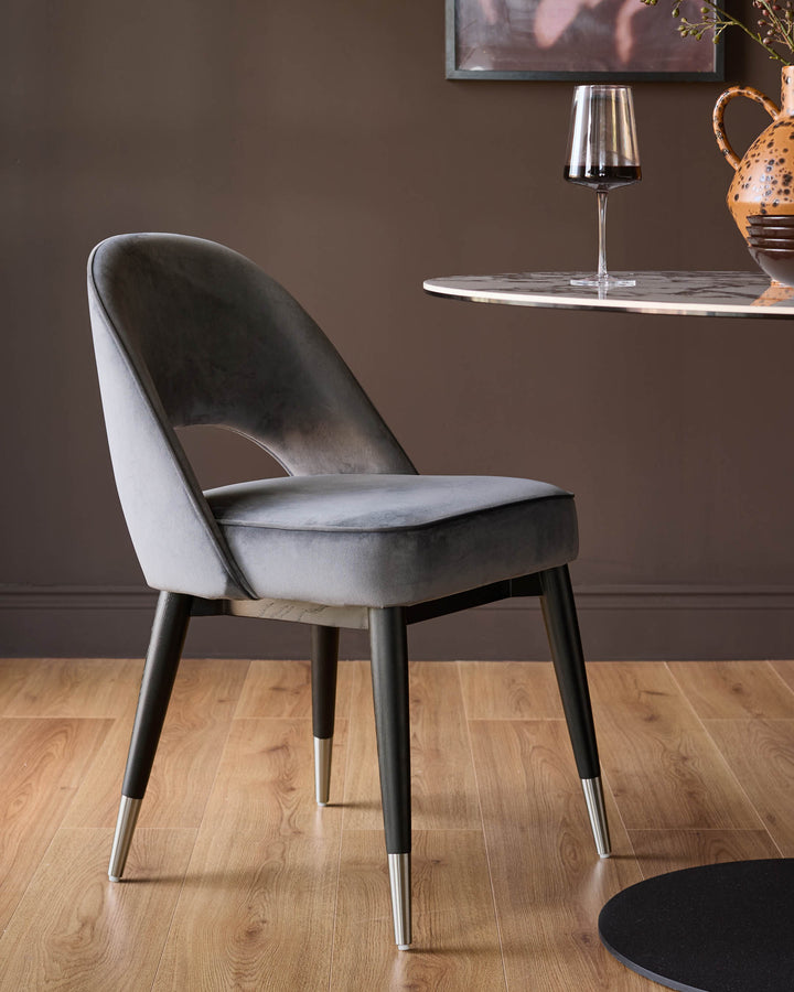 Dark grey velvet dining chair with curved backrest and stainless steel leg caps on wooden flooring.