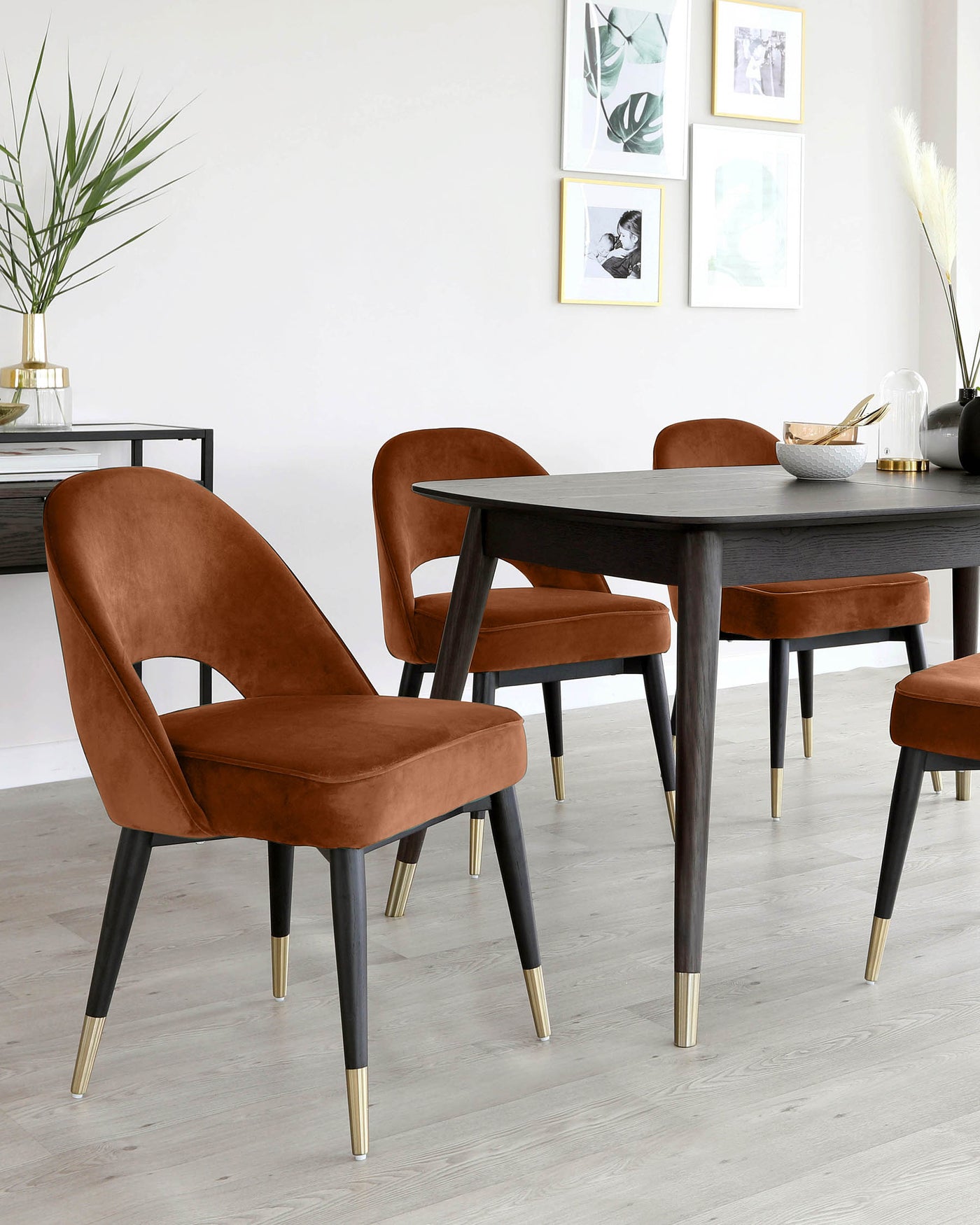 Elegant dining set featuring a modern, dark wood rectangular table with tapered legs, complemented by four luxurious caramel-coloured velvet upholstered chairs with sleek black legs accented with gold metal tips. The set exudes contemporary sophistication, ideal for a stylish interior.