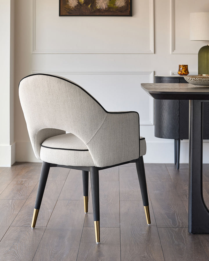 Clover Dining Armchair in ivory fabric with black curved backrest, black legs, and brass foot caps, shown in a styled room setting.