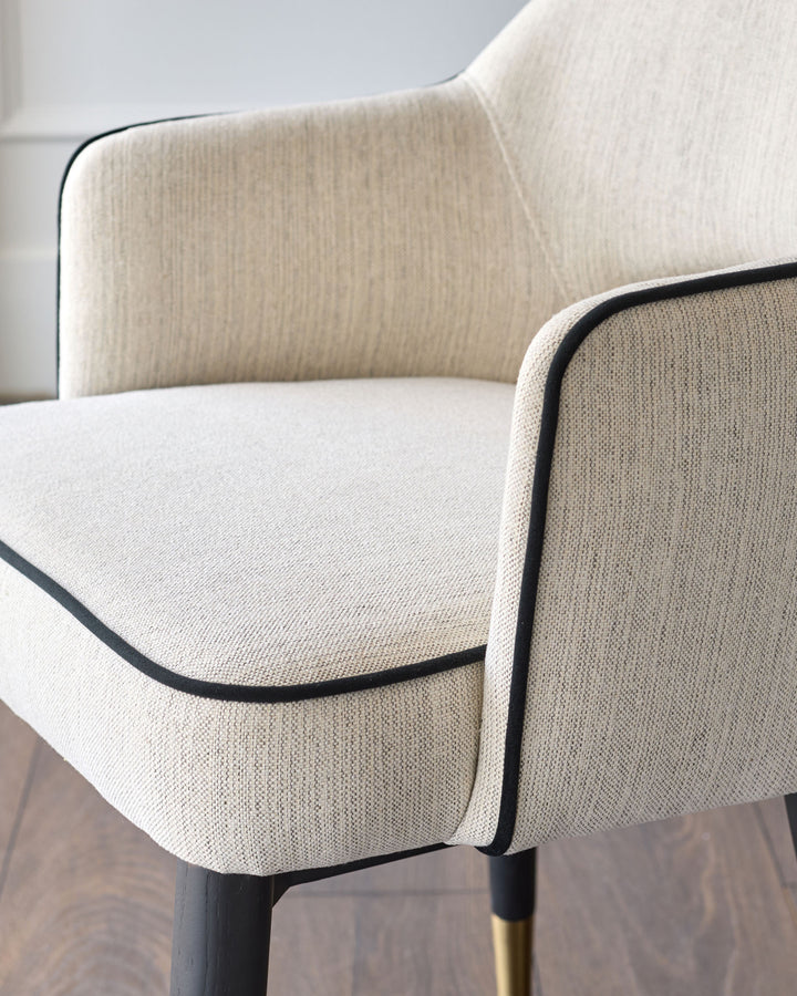 Clover dining armchair in ivory fabric, shown at close-up angle highlighting curved backrest and black piping detail.