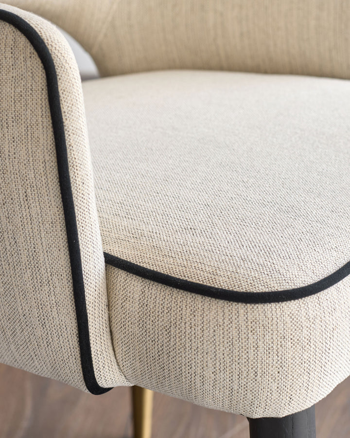 Clover dining armchair in ivory fabric, showing curved armrest detail with black piping trim and seat cushion from side angle.