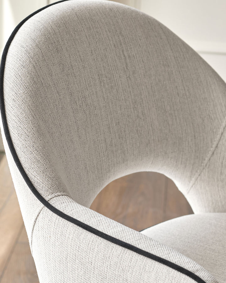 Clover dining armchair in ivory fabric, angled side view showing curved backrest and black trim detail.