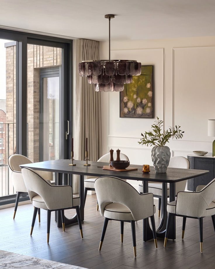 Ivory fabric dining armchair with curved back and brass-tipped legs, shown in modern dining room setting.