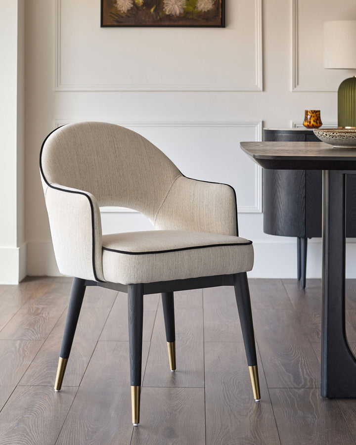Clover dining armchair in ivory fabric with black wooden legs and brass foot caps, shown in room setting.