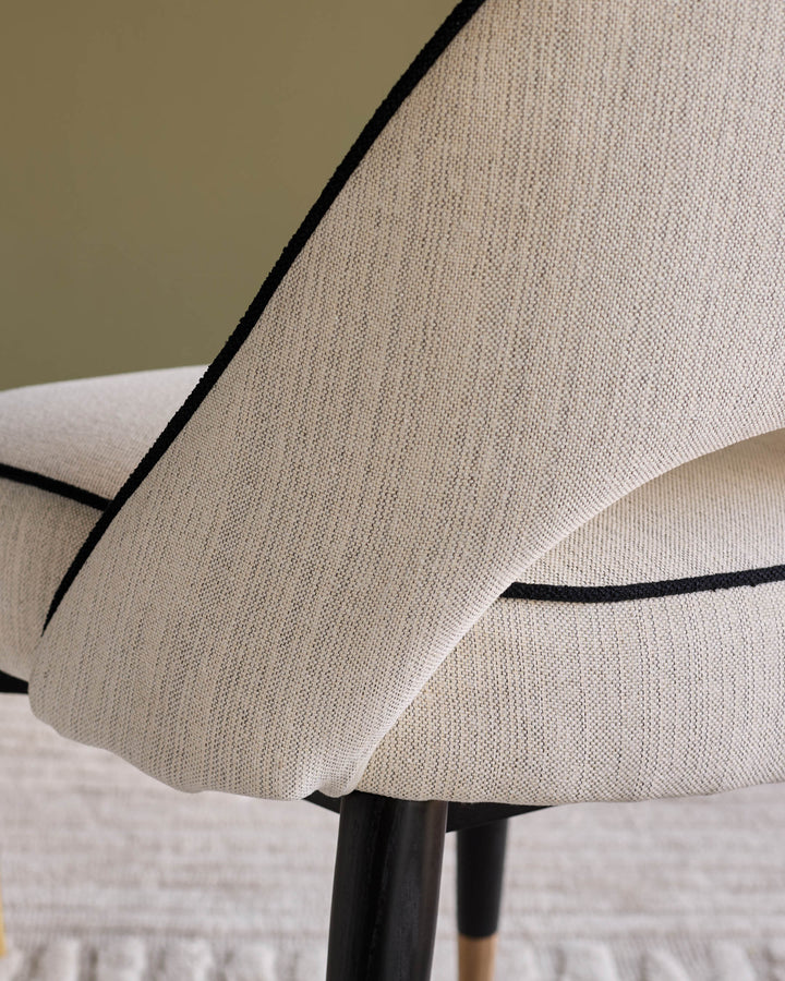 Clover Ivory Fabric Dining Chair - close-up side view showing curved backrest with black piping detail and wooden legs.