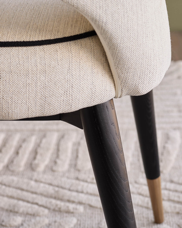 Clover fabric dining chair in ivory with black curved backrest and dark wooden legs with natural wood feet detail.