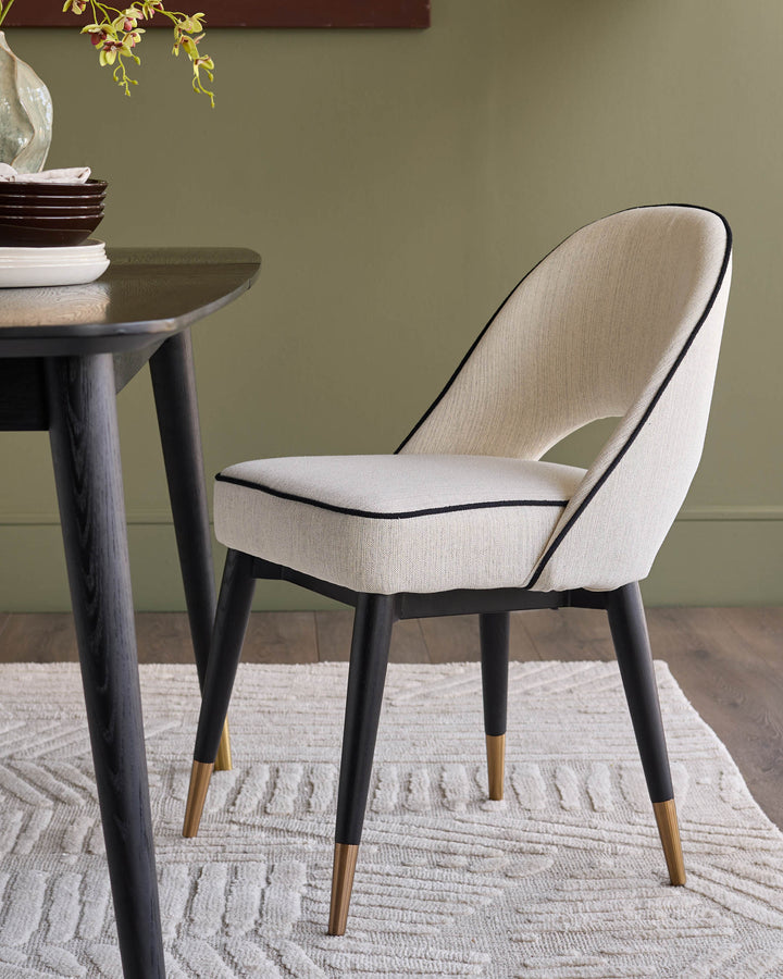 Clover ivory fabric dining chair with black piping, black legs, and brass foot caps, shown at a round dark wood table.