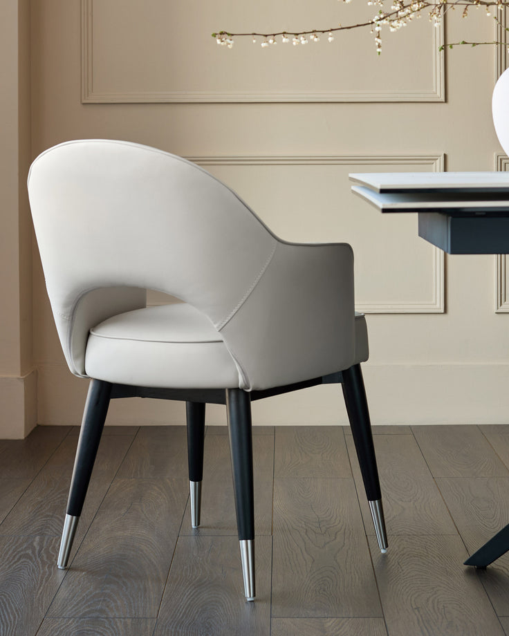 Clover dining armchair in light grey faux leather with black wooden legs and metal foot caps, shown in an elegant beige interior.