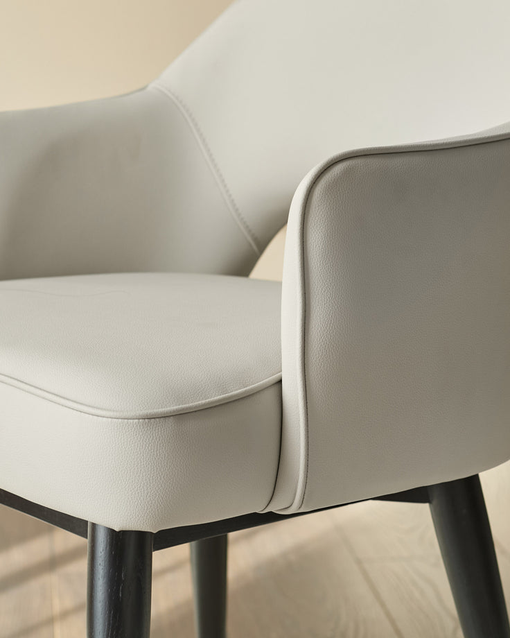 Clover dining armchair in light grey faux leather, close-up detail showing curved armrest and stitched seam with dark metal leg.