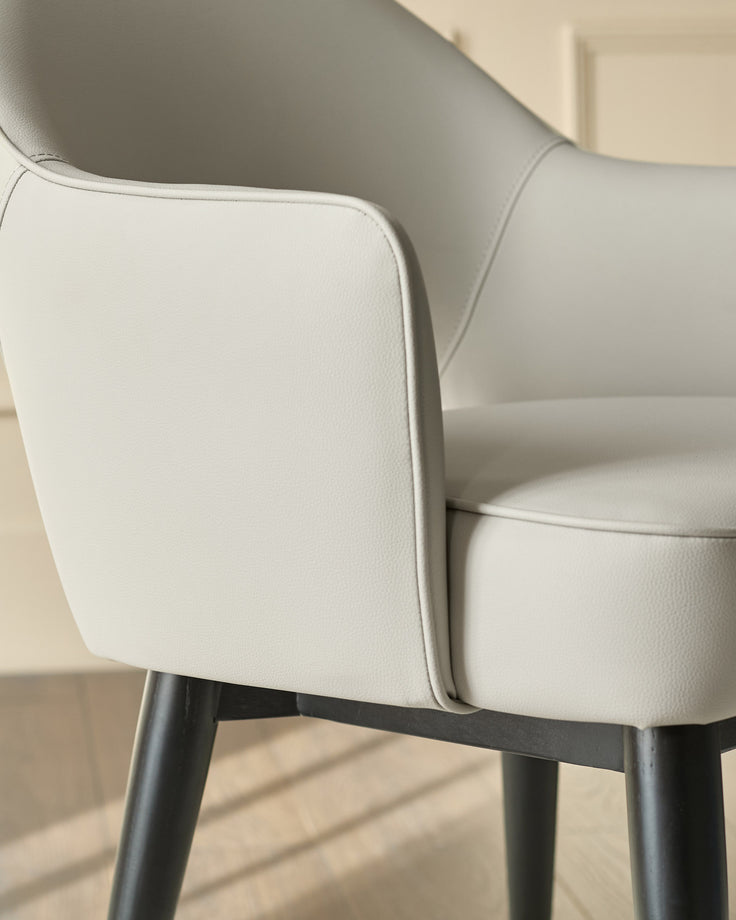 Clover dining armchair in light grey faux leather with black metal legs, shown in close-up detail of the backrest and armrest.