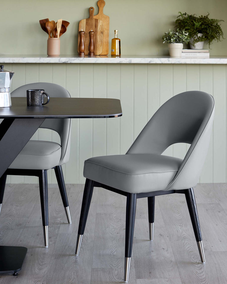 Modern minimalist furniture set featuring a sleek black round-edged rectangular table with a matte finish and solid black angled legs. Accompanied by a stylish, ergonomic grey chair with a curved backrest and padded seating, accentuated by black tapered legs with metallic tips. The set showcases a blend of industrial and contemporary design aesthetics, ideal for a chic dining area.