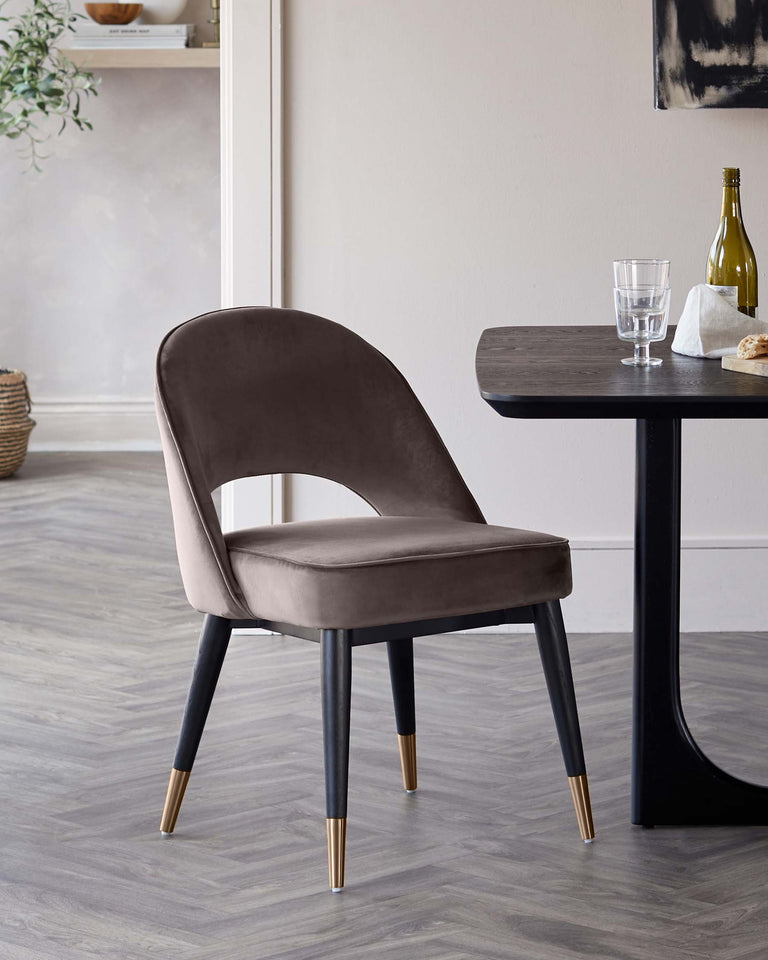 Elegant modern dining chair with smooth grey upholstery and black legs featuring gold-coloured tips, paired with a sleek black dining table with a rounded corner.