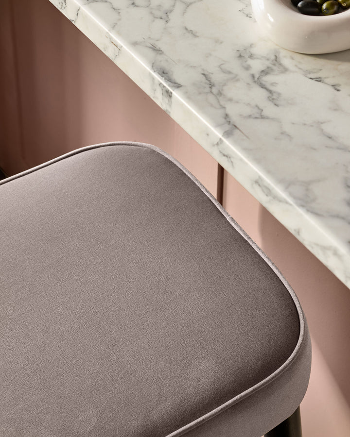 Mocha velvet backless bar stool with curved seat and piping detail, shown beside marble countertop.