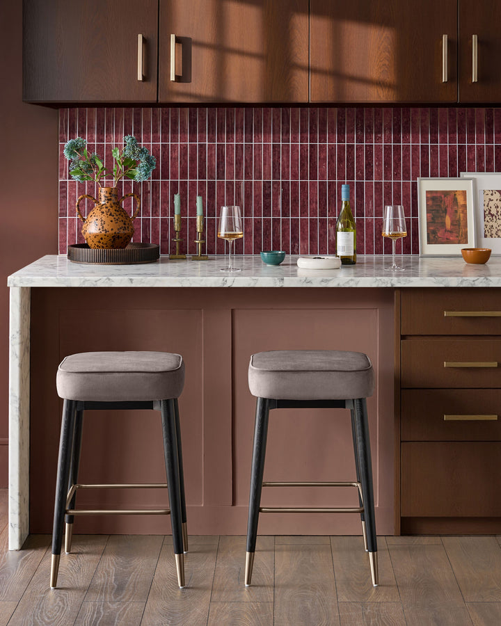 Mocha velvet backless bar stool with black legs and brass footrest, shown as pair at marble kitchen island.