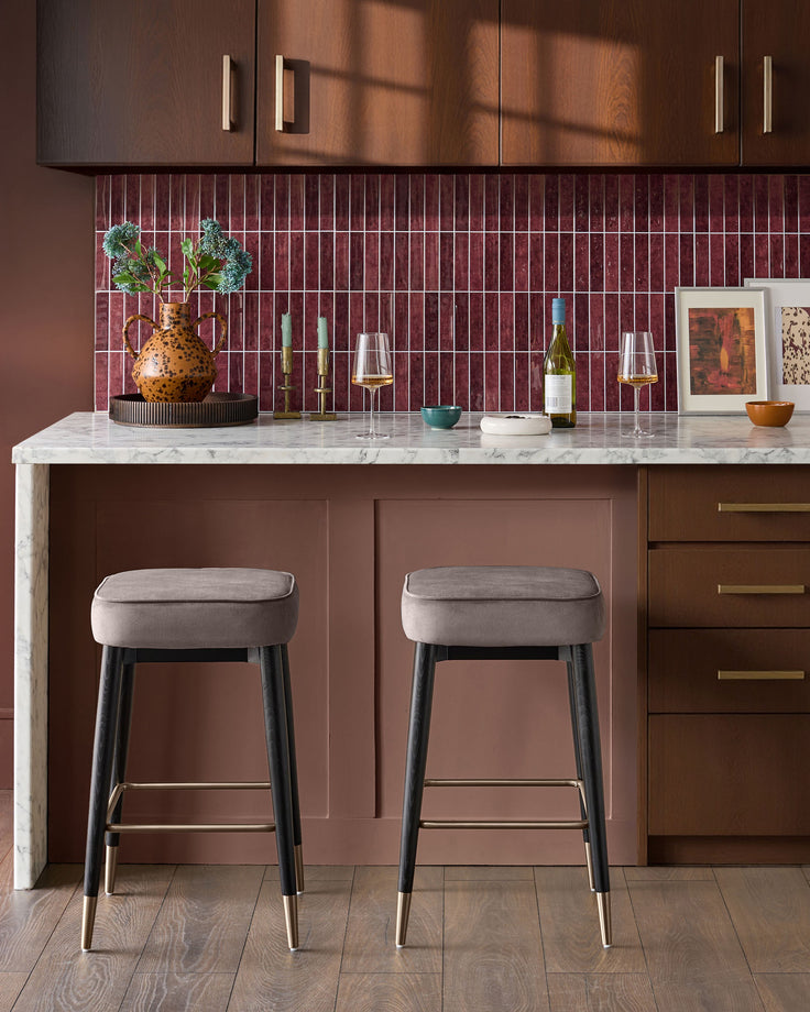Mocha velvet backless bar stool with black legs and brass footrest, shown as pair at marble kitchen island.