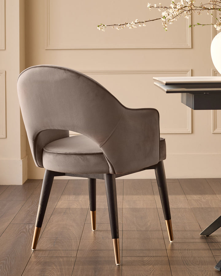Mocha velvet dining armchair with curved backrest and black wooden legs with brass-tipped feet, angled view.