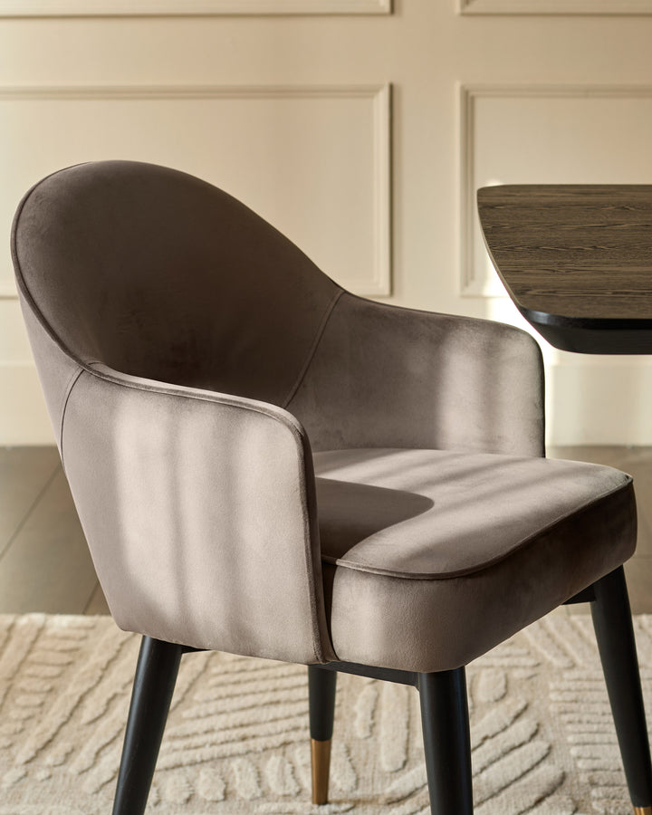 Mocha velvet dining armchair with curved backrest and black wooden legs with gold accents, angled side view.