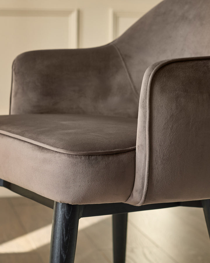 Clover velvet dining armchair in mocha, side angle showing curved backrest and black wooden legs.