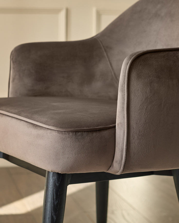 Clover velvet dining armchair in mocha, side angle showing curved backrest and black wooden legs.