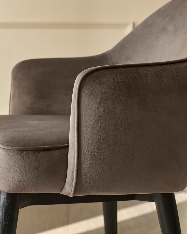 Clover velvet dining armchair in mocha, showing curved backrest and armrest detail with black wooden legs.