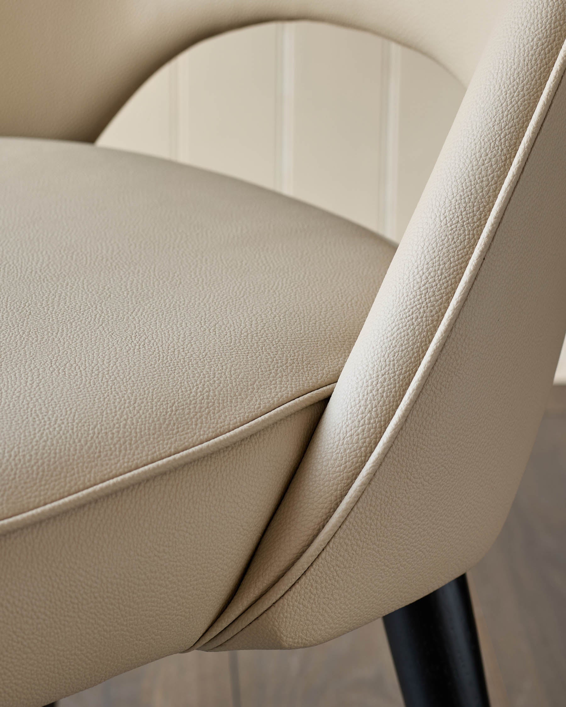 Close-up of a stylish, modern chair with cream leather upholstery and sleek black legs, showcasing its elegant design and comfort.