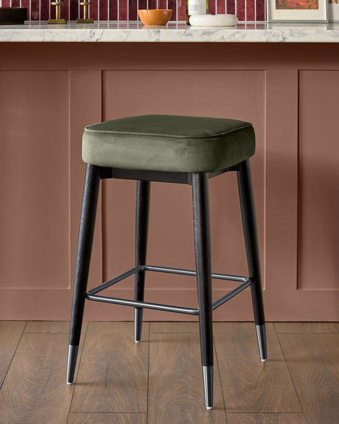 Clover velvet backless bar stool in olive green with dark wood legs and metal footrest.